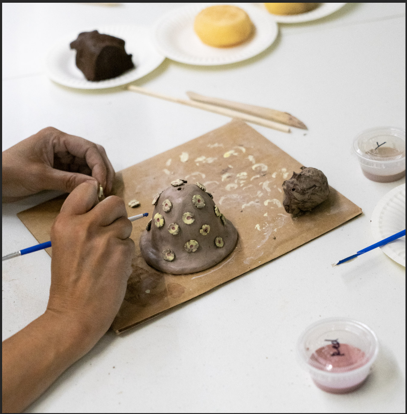 hands working with a brush and clay to make ceramic bells during the workshop