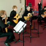 Four musicians sitting in chairs and playing music on guitars.