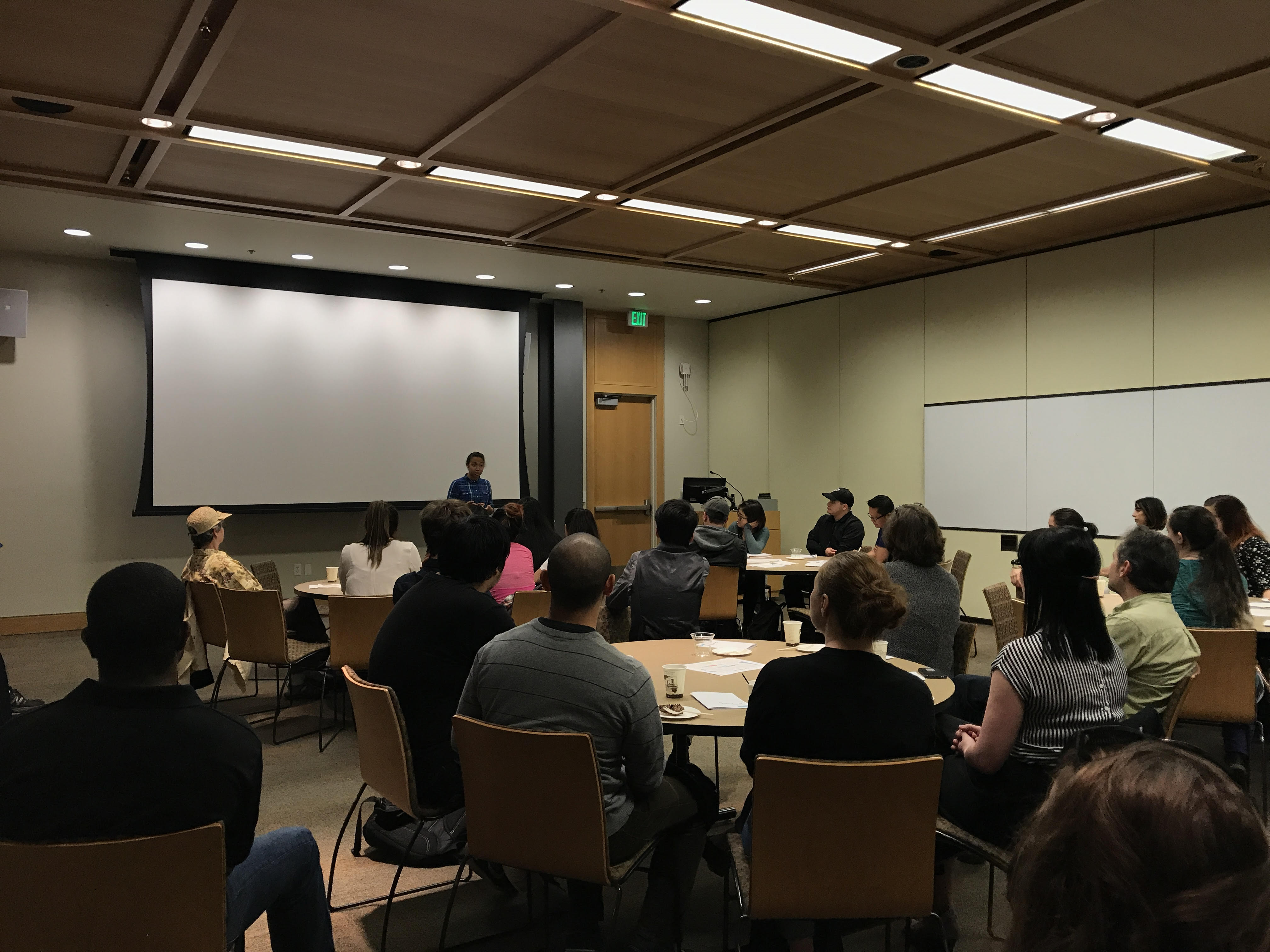 Students sitting around tables listening to a presentation.