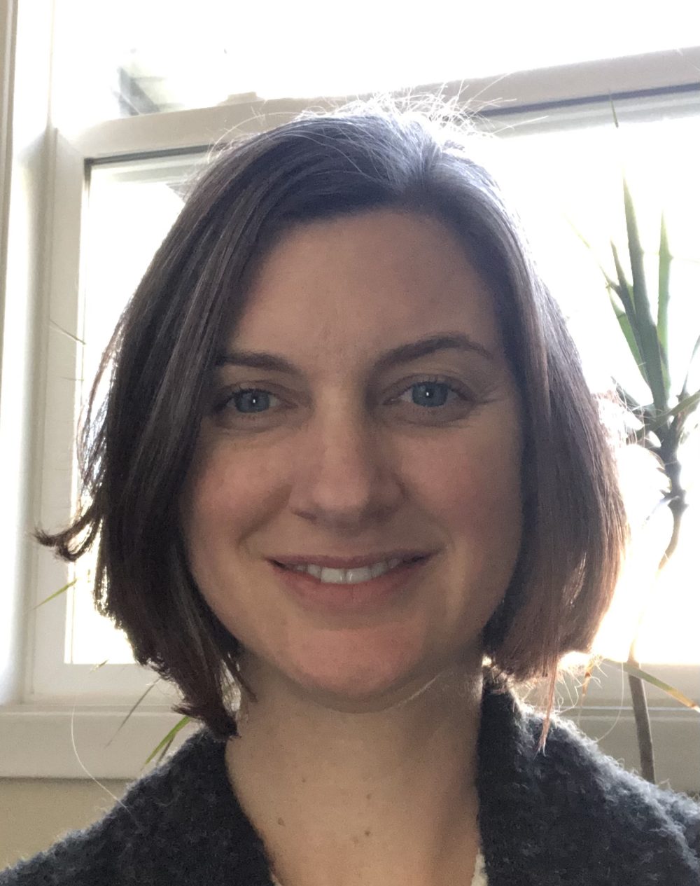 White woman with short brown hair and blue eyes, smiling.