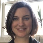 White woman with short brown hair and blue eyes, smiling.