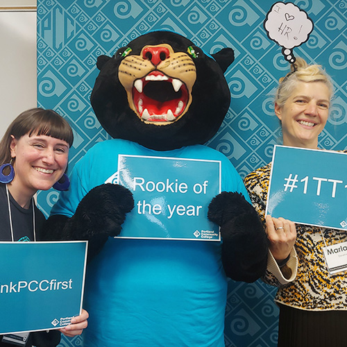 Poppie the Panther with two people holding PCC-branded signs