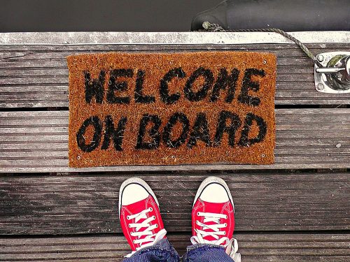 A person's shoes approaching a welcome mat that reads "Welcome On Board"