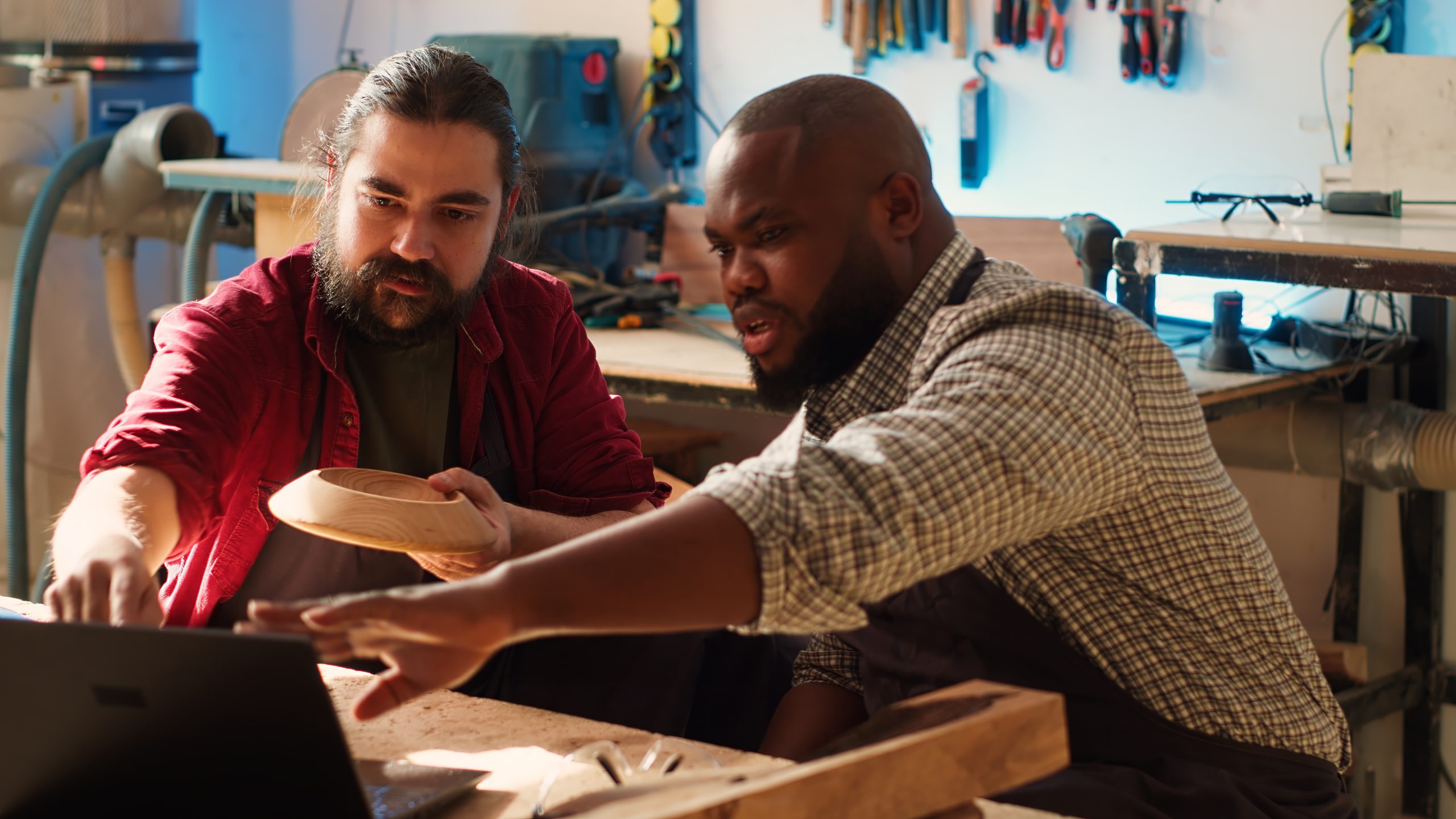 Woodworkers looking over blueprints on laptop, brainstorming