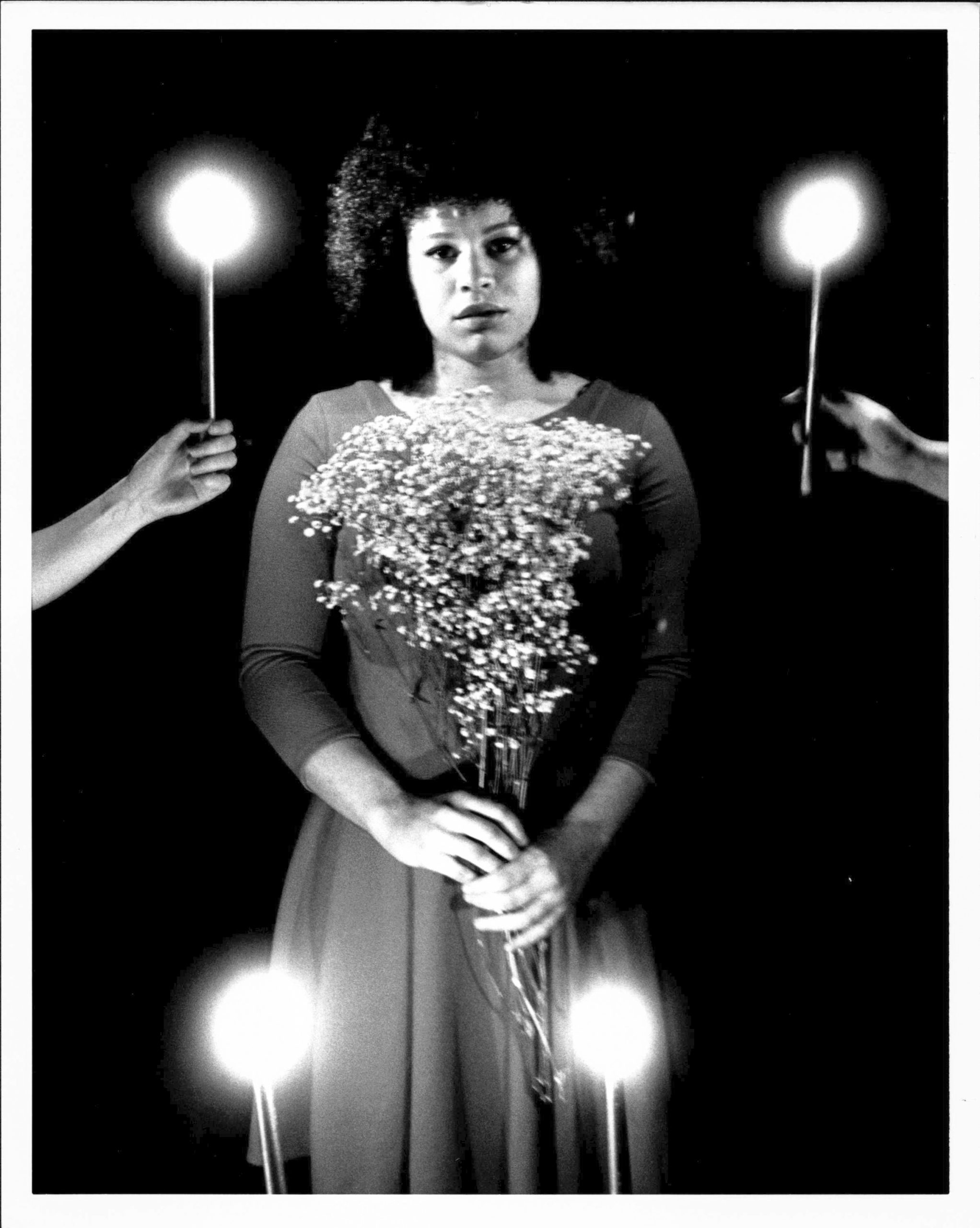 A woman stands with a bouquet. Four hands hold sparklers around her.
