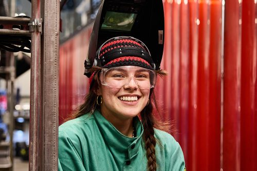 Female welding student wearing a helmet and smiling at the camera