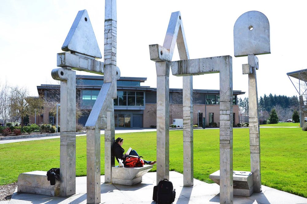 Student reading under a large sculpture on campus