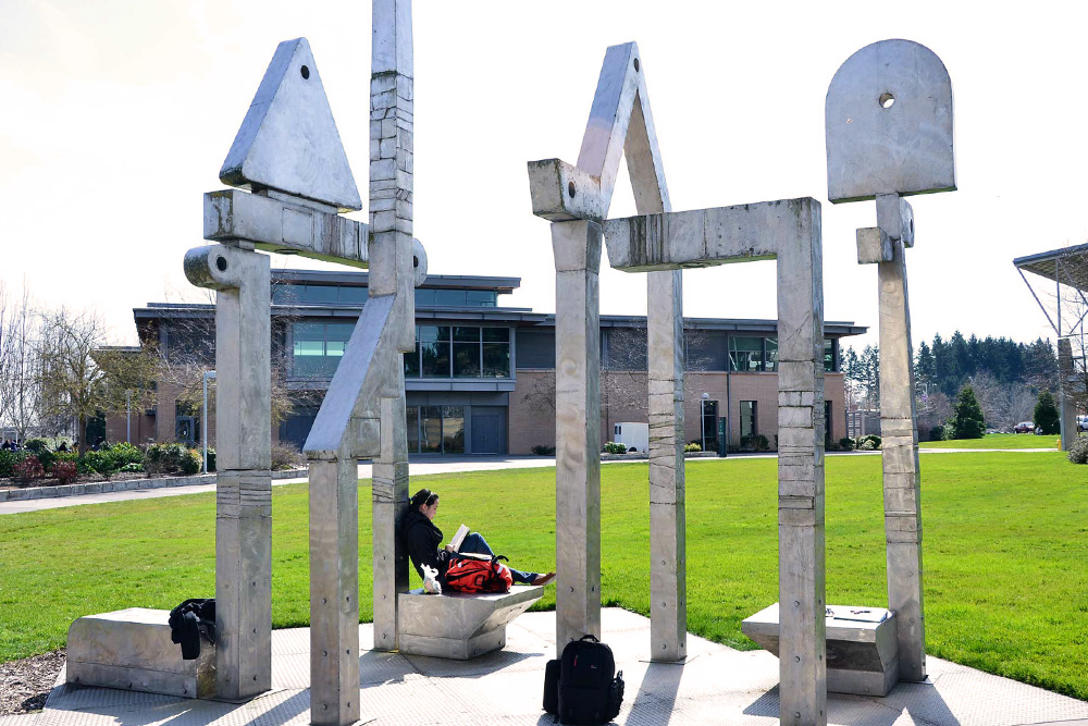 Student reading under a large sculpture on campus