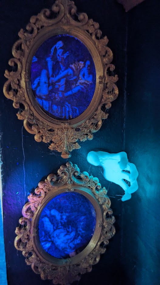 Glow in the dark hand coming out of the walls next to glowing paintings in the Haunted Dollhouse