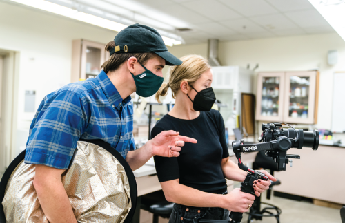A photo of two video production team members capturing video in a classroom.