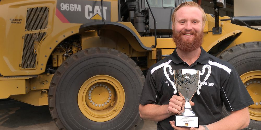 Ryan Walker holding his trophy in front of a CAT