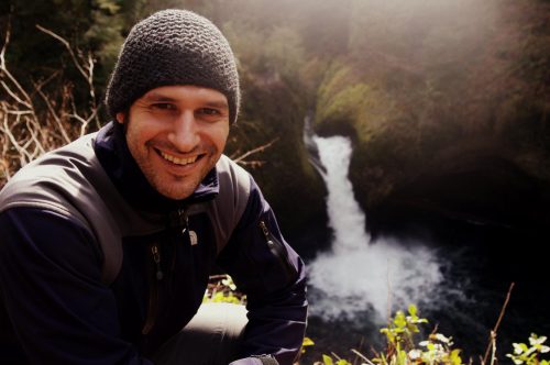 man wearing knit cap posing with waterfall in background