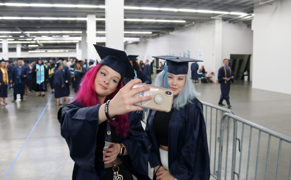 Two female grads take a cell phone selfie.