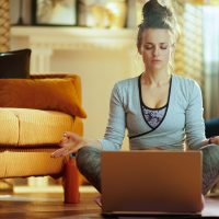 relaxed healthy sports woman in fitness clothes at modern home meditating using online streaming yoga site in laptop.