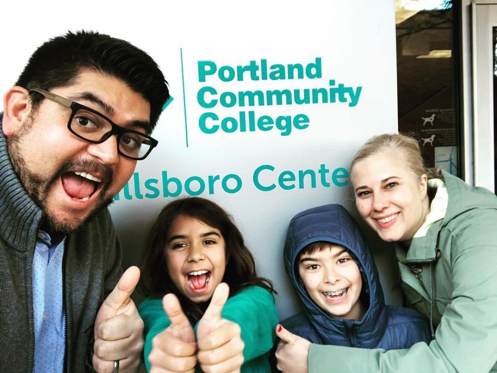 Family posed giving thumbs up and smiling in front of PCC Hillsboro Center sign
