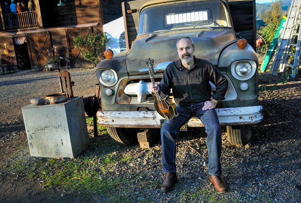 man holding mandolin sitting on an old truck