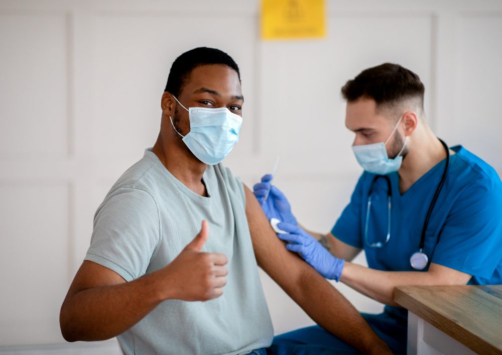 African American man in mask gesturing thumb up during coronavirus vaccination, approving of covid-19 immunization