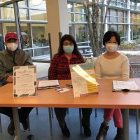 3 people sitting at a table wearing masks with informational materials