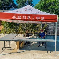 Two people sitting under a tent with the Oregon Chinese Coalition logo and other words in Chinese