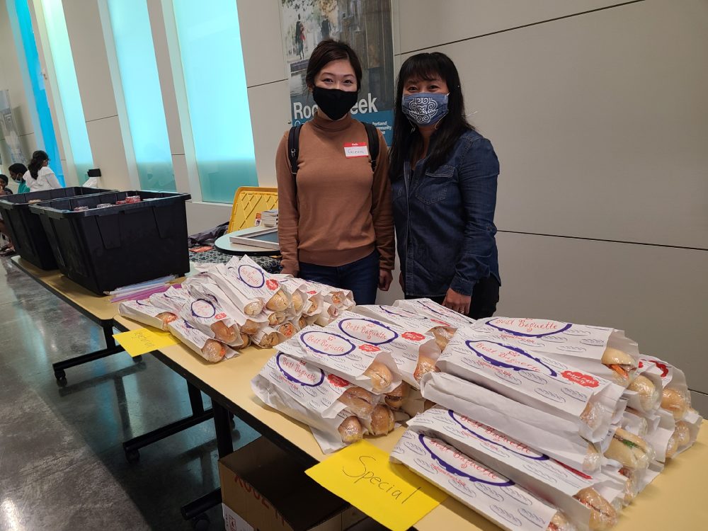 Two people standing behind a table. The table is filled with banhmi baguette sandwiches.