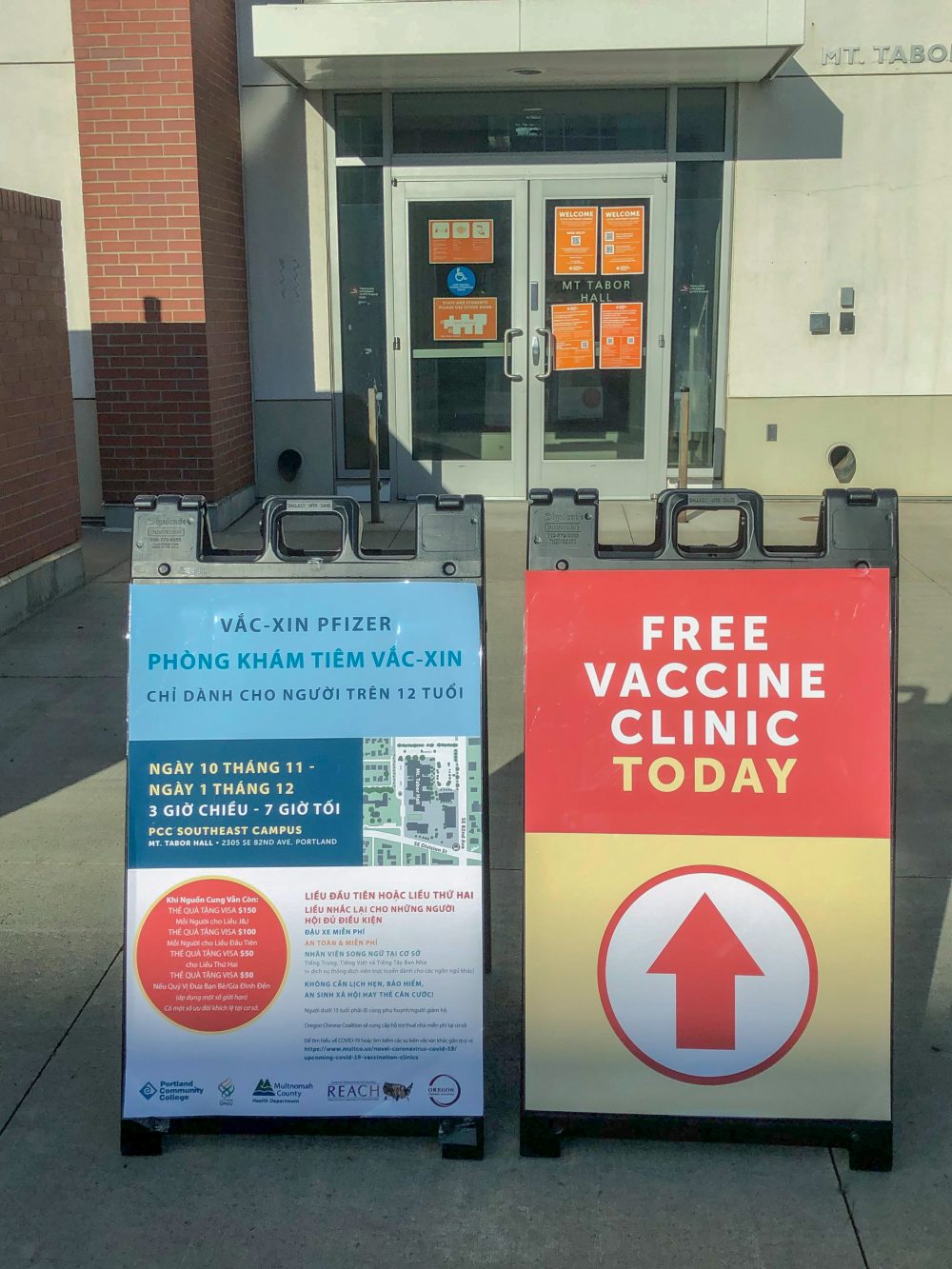 Sandwich boards that say free vaccine clinic today in English and all clinic details in Vietnamese