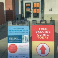 Sandwich boards that say free vaccine clinic today in English and all clinic details in Vietnamese