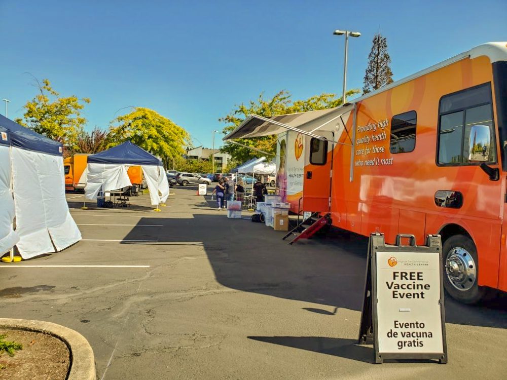 Mobile health truck with Virginia Garcia Memorial logo and a sandwich board with the words free vaccine event in English and Spanish