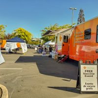 Mobile health truck with Virginia Garcia Memorial logo and a sandwich board with the words free vaccine event in English and Spanish