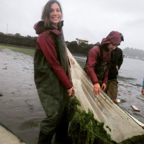 woman in waders smiling while pulling a net from the water