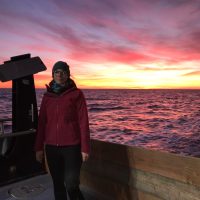 woman standing on the deck of a boat at sea at sunset