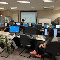 Tracee Wells standing at the front of a classroom filled with students and computers