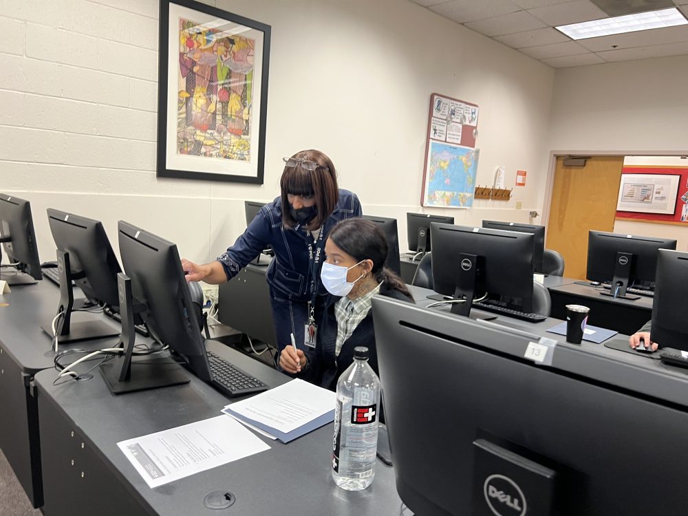 Tracee Wells standing at a computer assisting a student