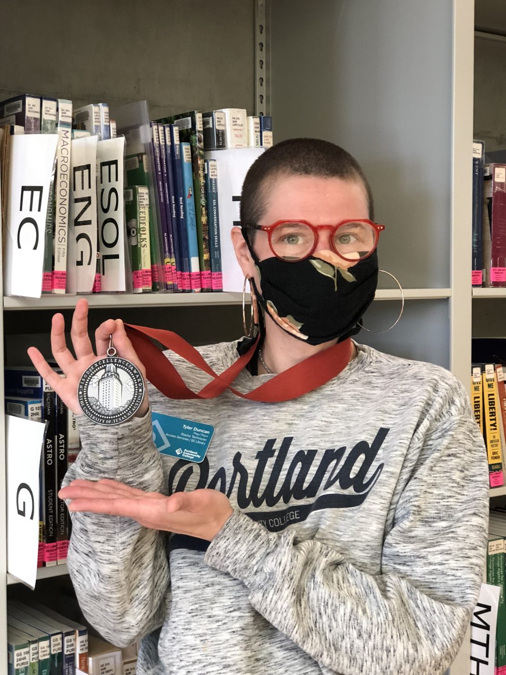 Tyler Duncan holds up award medal in front of book stacks