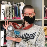 Tyler Duncan holds up award medal in front of book stacks
