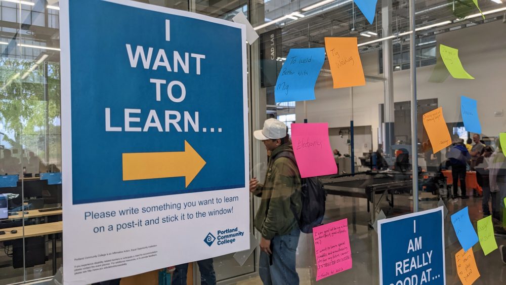 Sign reading "I Want to Learn" with arrow pointing to glass wall and brainstorm post-it notes