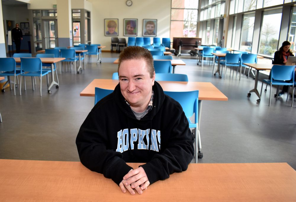 Neamhain Virtue seated at chair in SE Campus commons area.