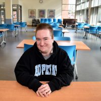 Neamhain Virtue seated at chair in SE Campus commons area.