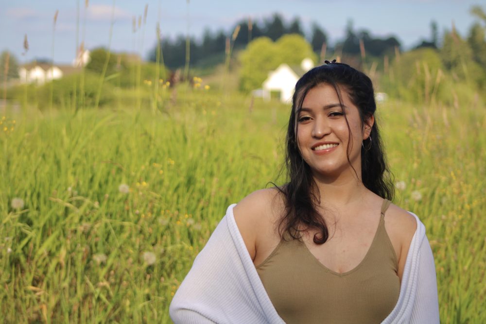 Young woman stands tall, smiling in a field.