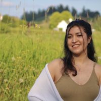 Young woman stands tall, smiling in a field.