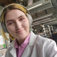 Young woman scientist wearing white lab coat and headphones in a lab.