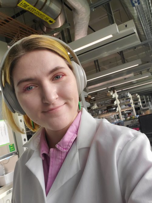 Young woman scientist wearing white lab coat and headphones in a lab.