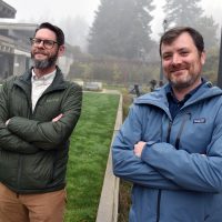 Adam Holzschuh and Eric Brurud in front of HT courtyard, arms folded.