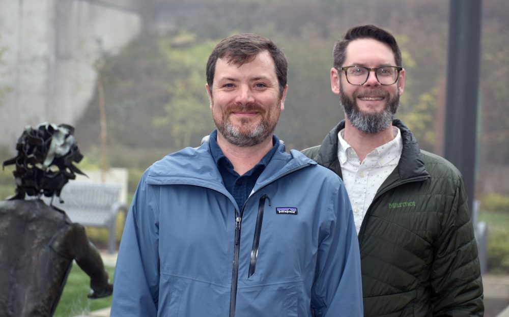 Adam Holzschuh and Eric Brurud in front of HT courtyard, arms folded.