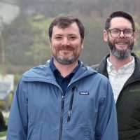 Adam Holzschuh and Eric Brurud in front of HT courtyard, arms folded.