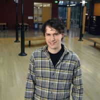 Man in flannel stands in PCC building smiling.