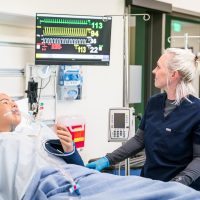 Nursing student in training lab with manikin patient.