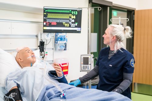 Nursing student in training lab with manikin patient.