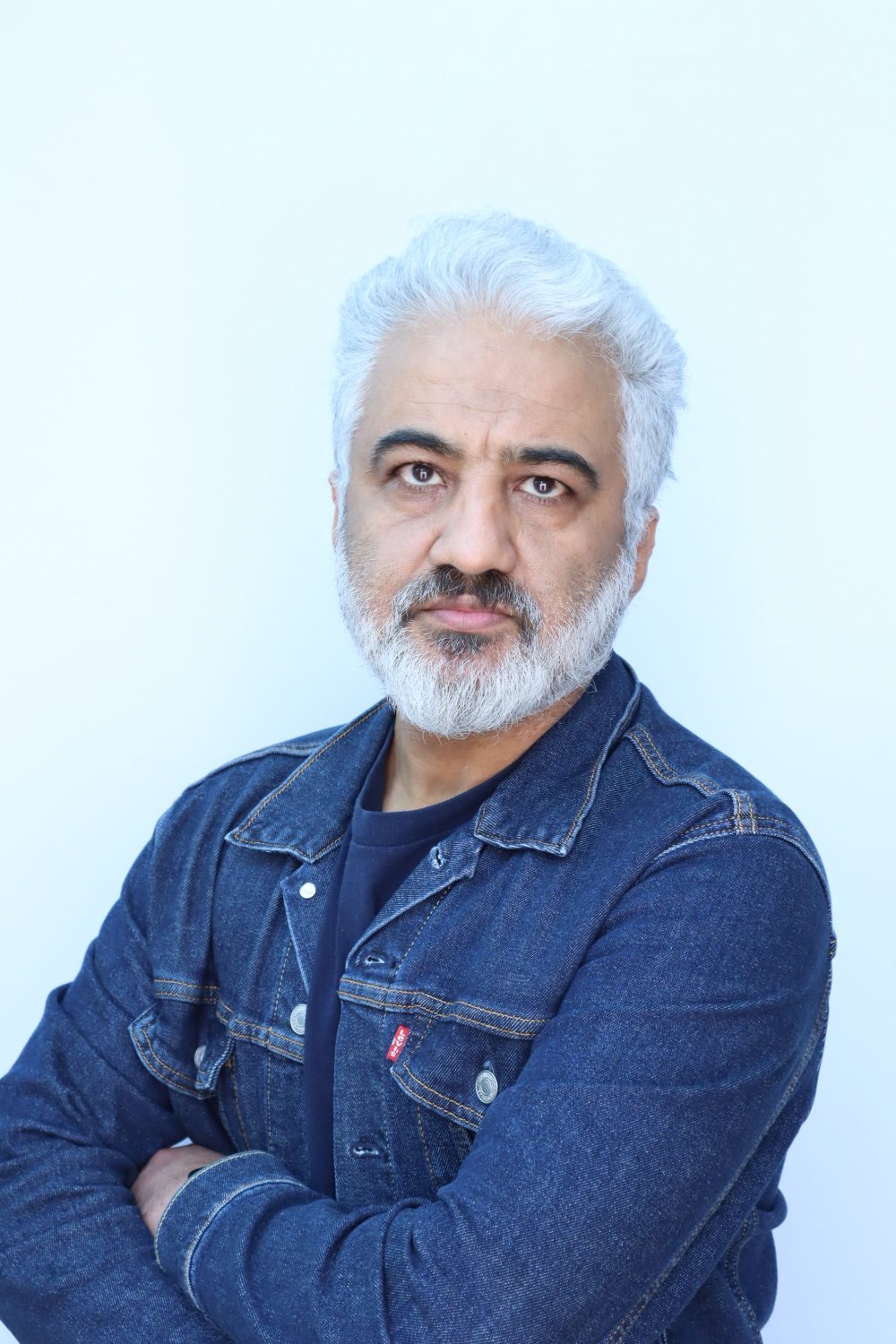 Gray-haired, bearded man in denim shirt looks at camera.