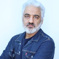 Gray-haired, bearded man in denim shirt looks at camera.