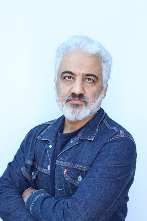 Gray-haired, bearded man in denim shirt looks at camera.